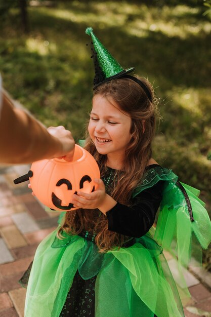 Schattig klein meisje in een groen Halloween-kostuum van een heks of fee met een pompoenmand voor snoep