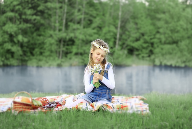 Schattig klein meisje in een krans en een boeket wilde bloemen op een picknick in het bos