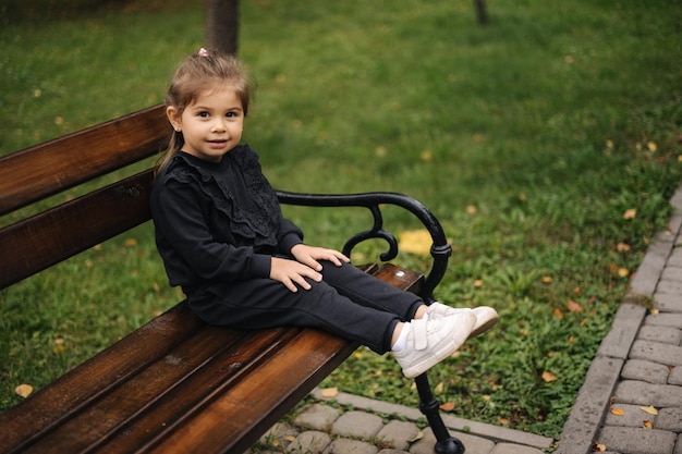 Schattig klein meisje in een mooi zwart pak zittend op de bank herfststemming