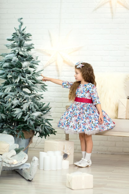 Schattig klein meisje in een mooie jurk poseren in de buurt van de kerstboom.