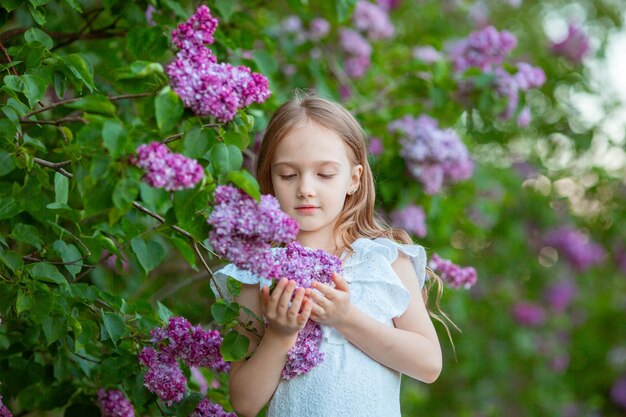 Schattig klein meisje in een witte jurk in een bloeiende lila lentetuin