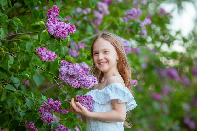 schattig klein meisje in een witte jurk in een bloeiende lila lentetuin