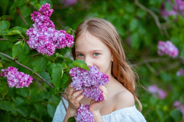 schattig klein meisje in een witte jurk in een bloeiende lila lentetuin