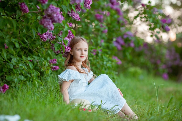 schattig klein meisje in een witte jurk in een bloeiende lila lentetuin