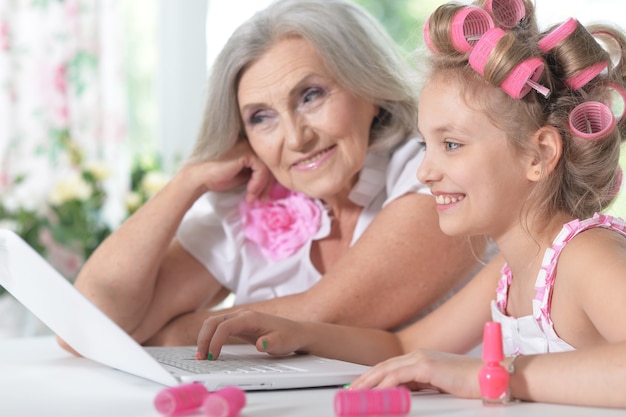 Schattig klein meisje in haarkrulspelden met oma die laptop thuis gebruikt