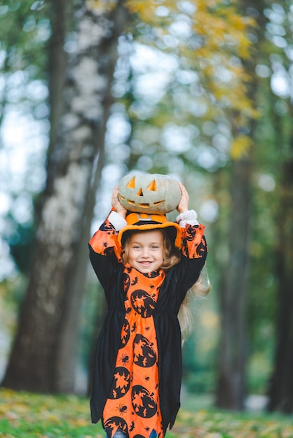 Schattig klein meisje in heksenkostuum voor de vakantie van Halloween. Ze houdt een pompoen in haar handen en staat in het park.