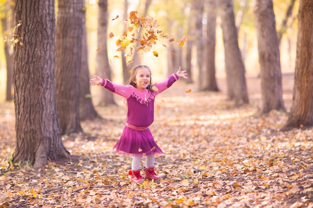 Schattig klein meisje in herfst park met oranje en gele kleur bladeren.