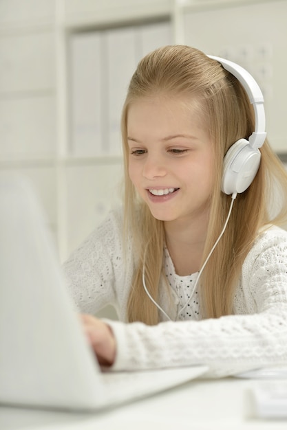 Schattig klein meisje in hoofdtelefoon met laptop en pen thuis