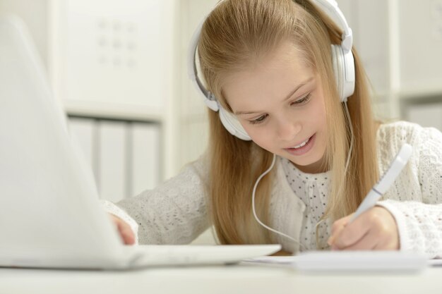 Schattig klein meisje in hoofdtelefoon met laptop en pen thuis