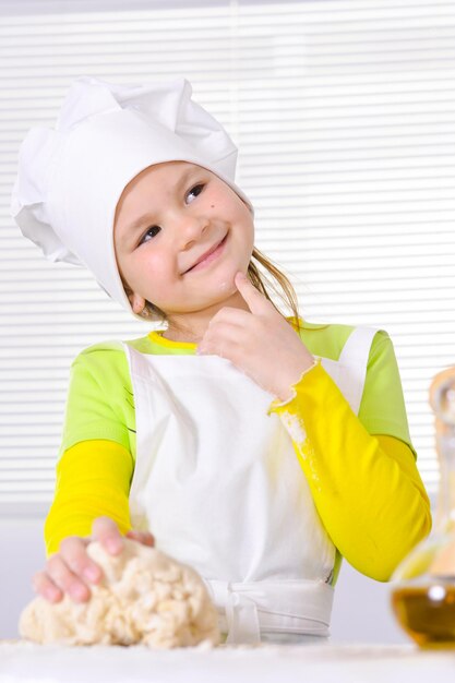 Schattig klein meisje in koksmuts taart bakken in de keuken