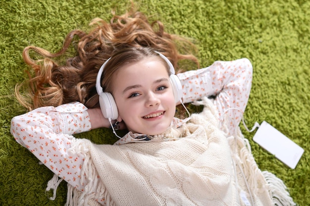 Schattig klein meisje in koptelefoon luisteren naar muziek terwijl liggend op groen tapijt