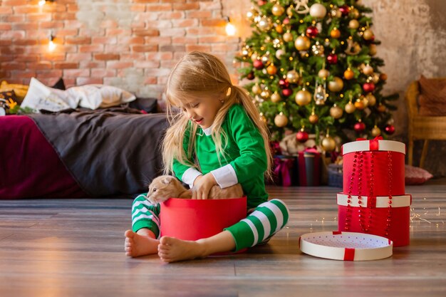 Schattig klein meisje in pyjama's in de buurt van de kerstboom