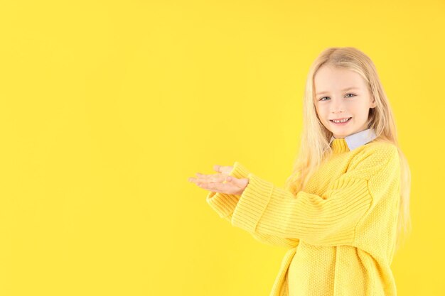 Schattig klein meisje in trui op gele achtergrond