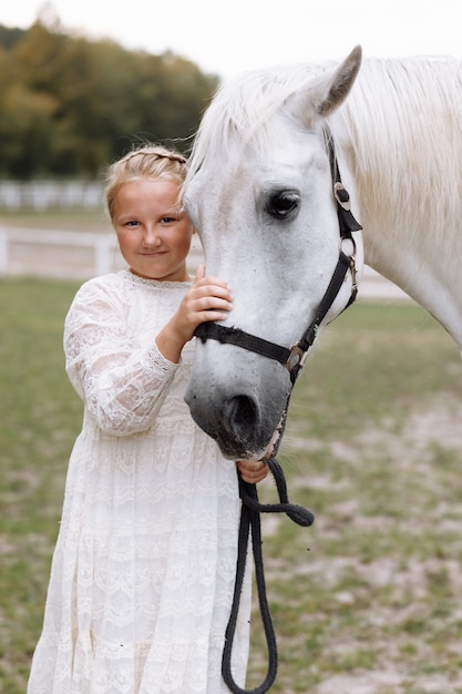 Schattig klein meisje in witte jurk een paard aaien op het platteland op de boerderij op een mooie zomerdag.