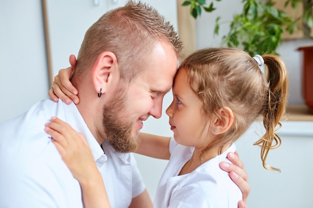 Schattig klein meisje in witte jurk knuffelen liefdevolle vader hem kijken met liefde en tederheid