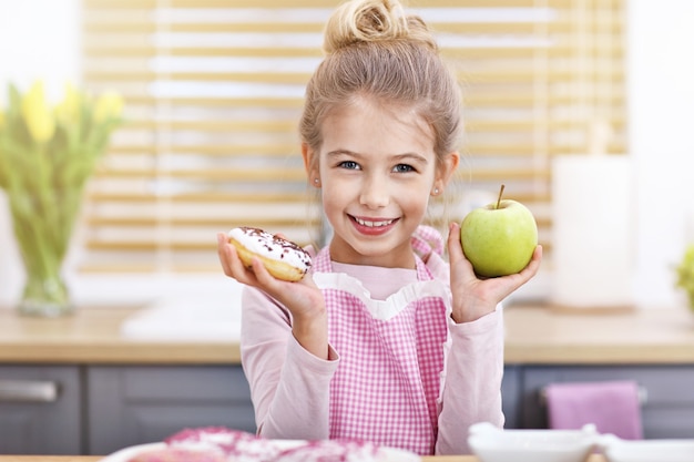 Schattig klein meisje kiezen tussen gezonde en ongezonde snack in de keuken