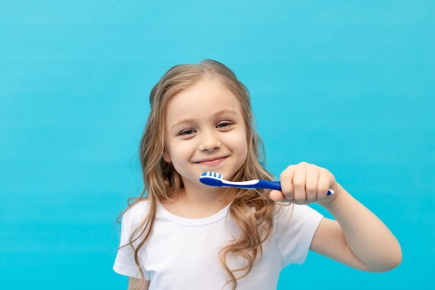 Schattig klein meisje kind in een wit T-shirt haar tanden poetsen met een tandenborstel op een blauwe achtergrond, het concept van hygiëne en tandheelkunde, ruimte voor tekst