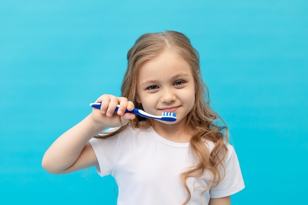 Schattig klein meisje kind in een witte T-shirt haar tanden poetsen met een tandenborstel op een blauwe achtergrond het concept van hygiëne en tandheelkunde ruimte voor tekst