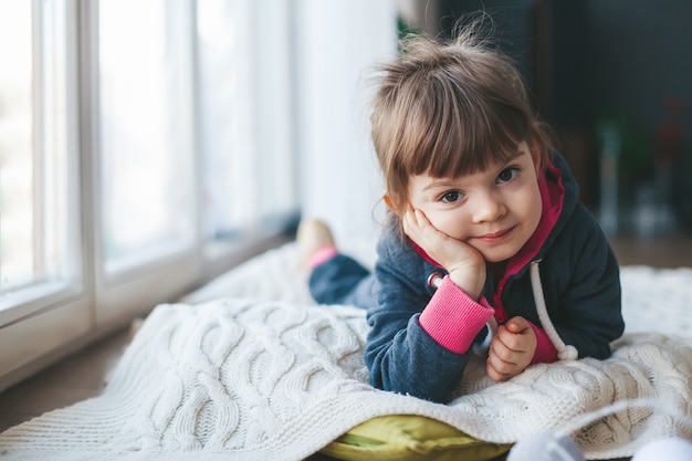 Schattig klein meisje liggend op een wollen deken bij het raam in de winter