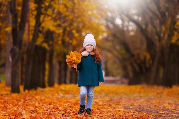 Schattig klein meisje met boeket gele bladeren in herfst park