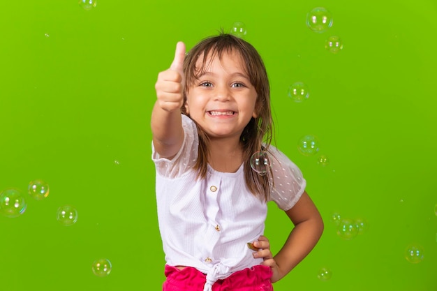 Schattig klein meisje met duim omhoog op groene achtergrond met zeepbellen