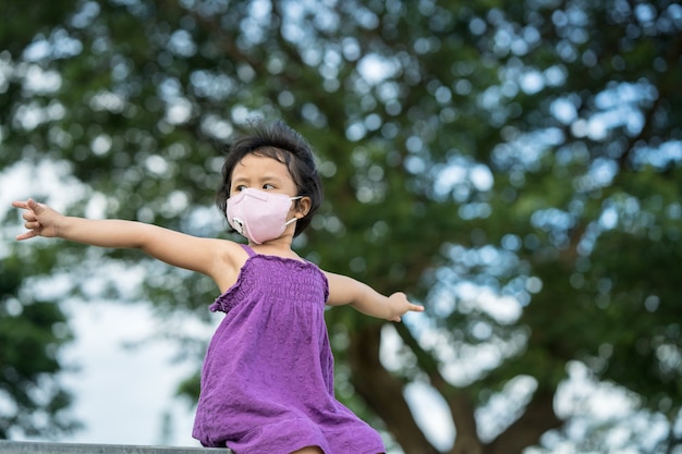 Schattig klein meisje met een beschermend gezichtsmasker dat tegen de regenboom zit