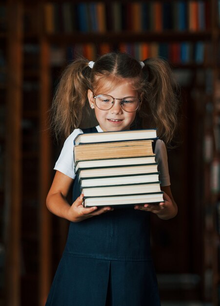 Schattig klein meisje met een bril staat in de bibliotheek vol boeken