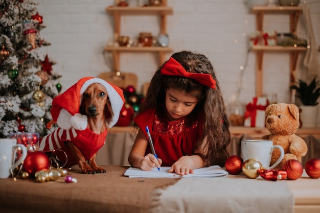 Schattig klein meisje met een dwerg teckel schrijft een brief met wensen aan het kerstconcept van de Kerstman