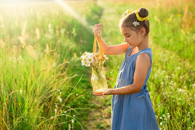 Schattig klein meisje met een gebreide tas met een boeket madeliefjes in een veld