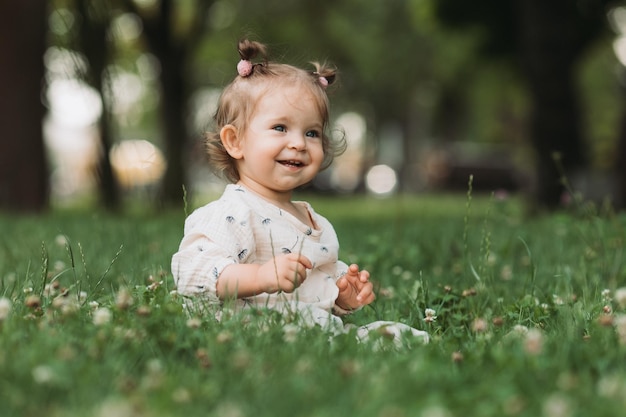 schattig klein meisje met een grappig kapsel zit op een bloeiend groen gazon in het park Lifestyle