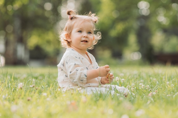 schattig klein meisje met een grappig kapsel zit op een bloeiend groen gazon in het park Lifestyle