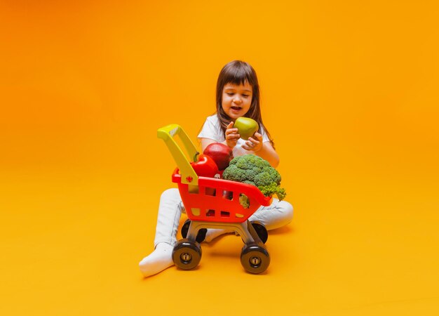 Schattig klein meisje met een mand met boodschappen uit een supermarkt geïsoleerd op een gele backgroundstudio photo