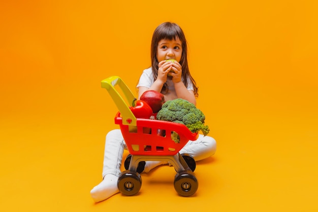 Schattig klein meisje met een mand met boodschappen uit een supermarkt geïsoleerd op een gele backgroundstudio photo