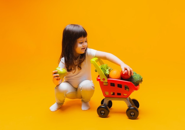 Schattig klein meisje met een mand met boodschappen uit een supermarkt geïsoleerd op een gele backgroundstudio photo