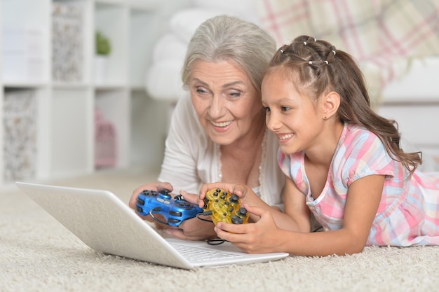 Schattig klein meisje met haar grootmoeder die computerspel speelt met laptop