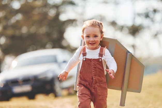 Schattig klein meisje met handgemaakte vleugels die buiten op het veld rennen en plezier hebben