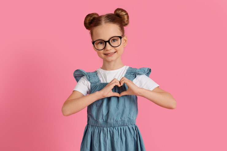 Schattig klein meisje met hart gebaar met handen in de buurt van de borst