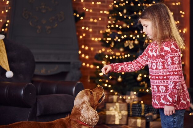 Schattig klein meisje met hond samen in de kerst ingerichte kamer.