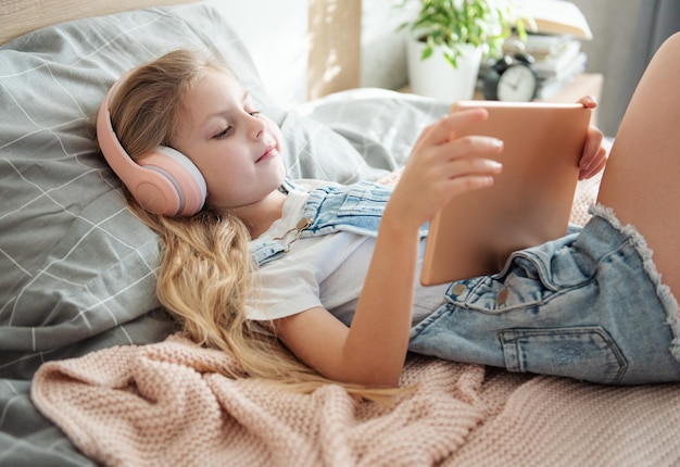 Schattig klein meisje met koptelefoon gebruikt thuis een tablet