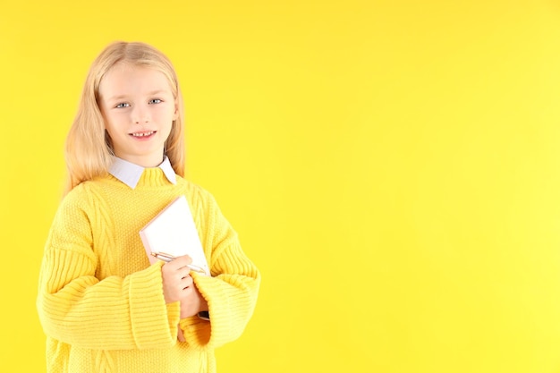 Schattig klein meisje met notitieboekje en pen op gele achtergrond