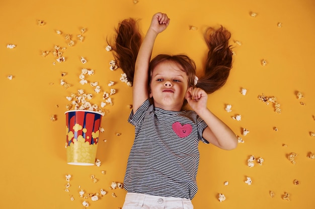 Schattig klein meisje met popcorn liggend op de gele vloer.