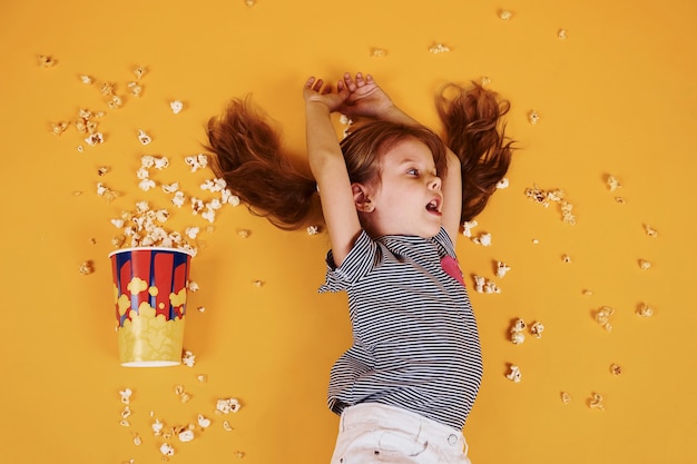 Schattig klein meisje met popcorn liggend op de gele vloer.