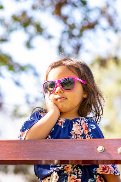 Schattig klein meisje met roze zonnebril en handen op haar gezicht.