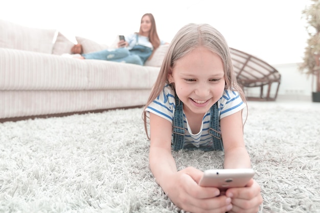 Schattig klein meisje met smartphone liggend op het tapijt in de woonkamer