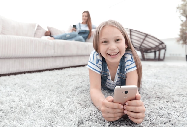 Schattig klein meisje met smartphone liggend op het tapijt in de woonkamerfoto met kopieerruimte