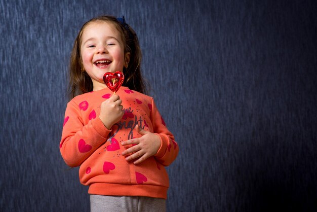 Schattig klein meisje met snoep in de vorm van een hart op de blauwe achtergrond