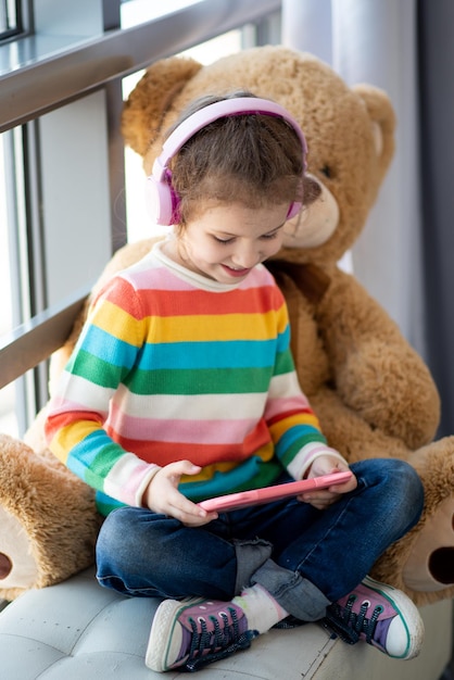 Schattig klein meisje met tabletcomputer in haar handen Ze zit in een koptelefoon Kinderen gebruiken technologie