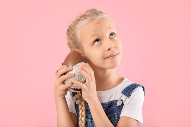 Schattig klein meisje met zoete chocolade-ei op kleur achtergrond