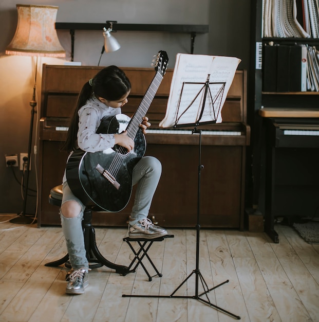 Schattig klein meisje oefenen op een akoestische gitaar thuis