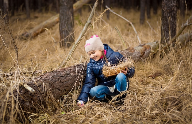 Schattig klein meisje op zoek naar paaseieren onder een boomstam in het bos